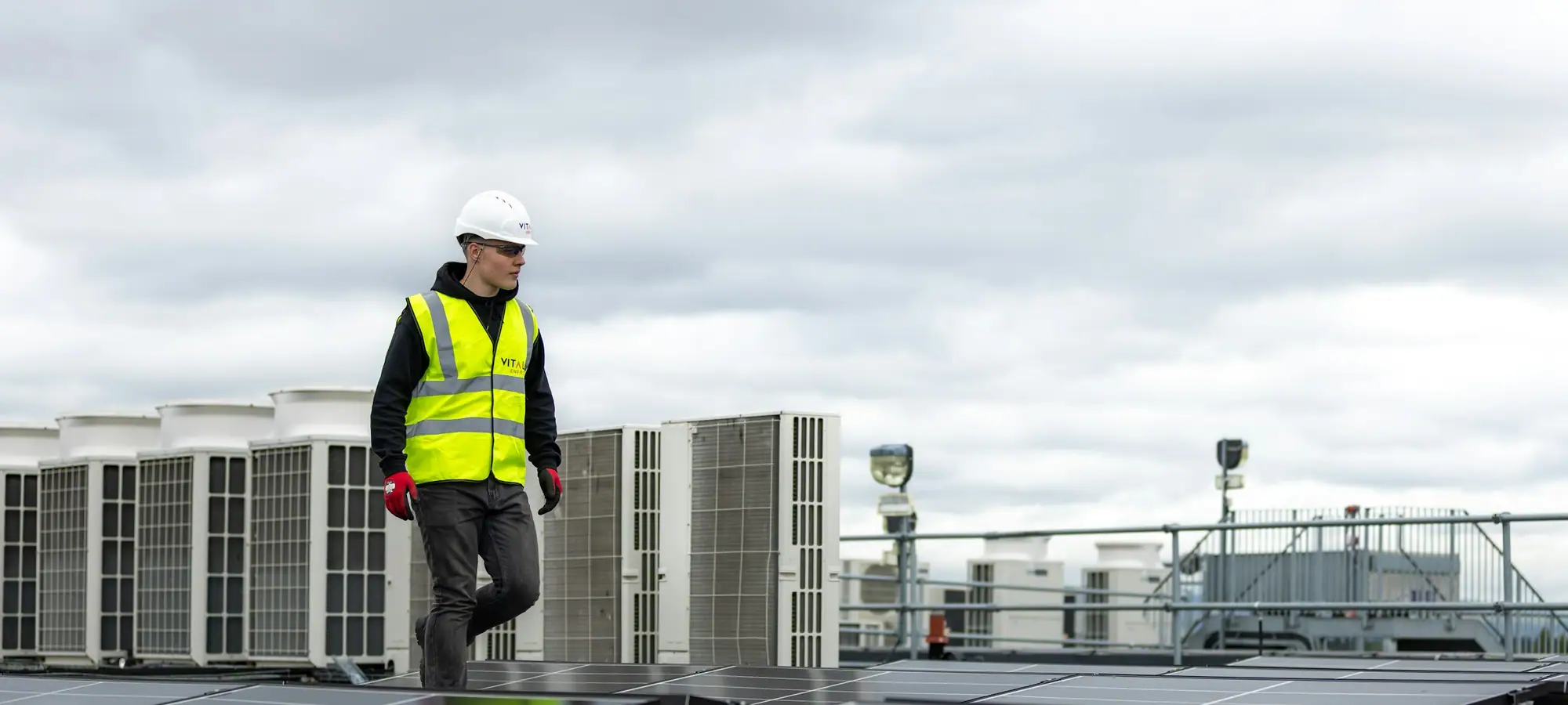 Technician in a safety vest walking a commercial rooftop lined with mechanical units