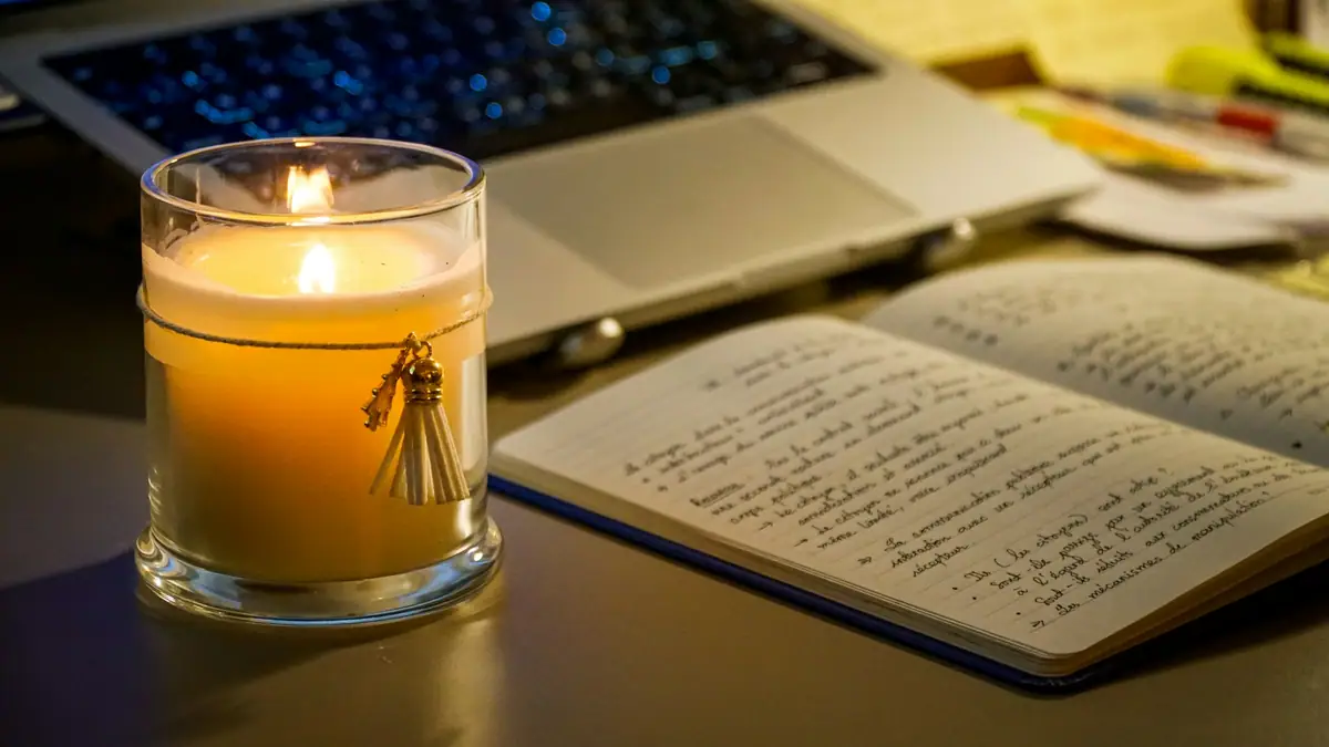 Candle beside an open handwritten notebook and laptop