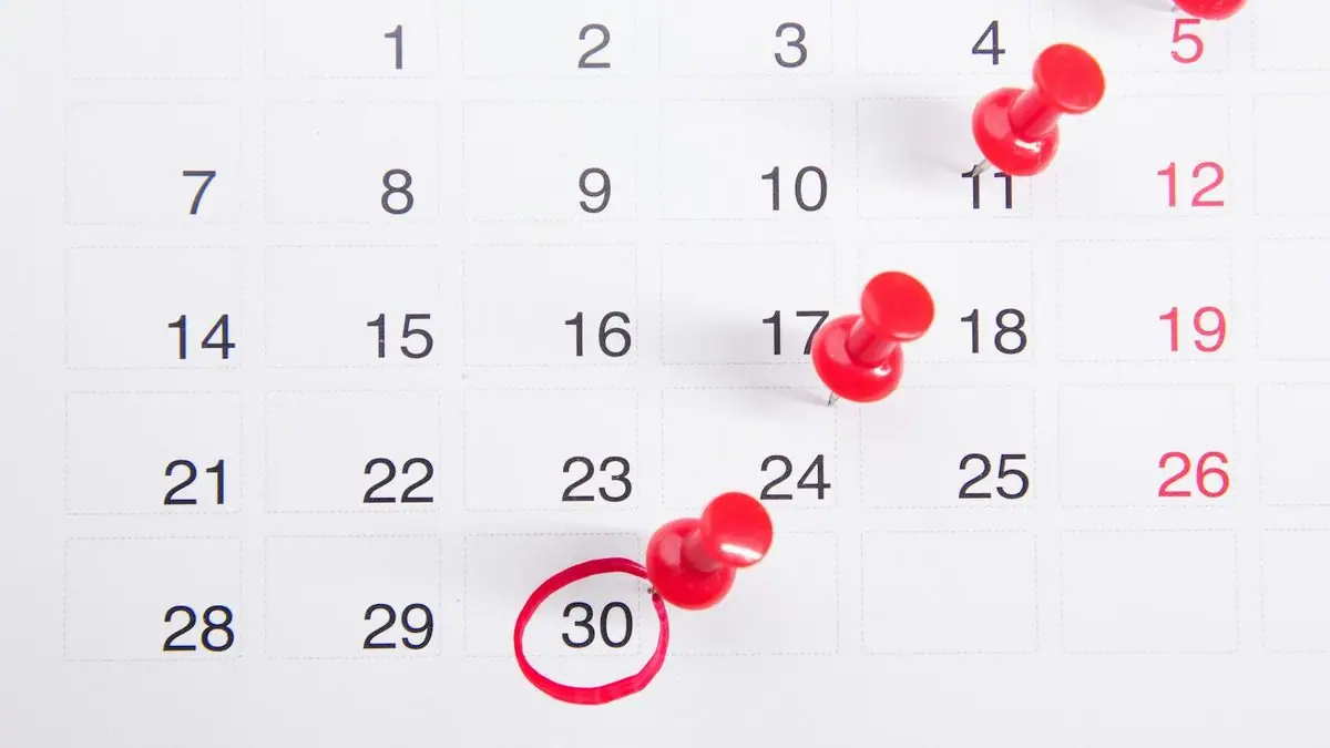 Red push pins marking dates on a monthly calendar
