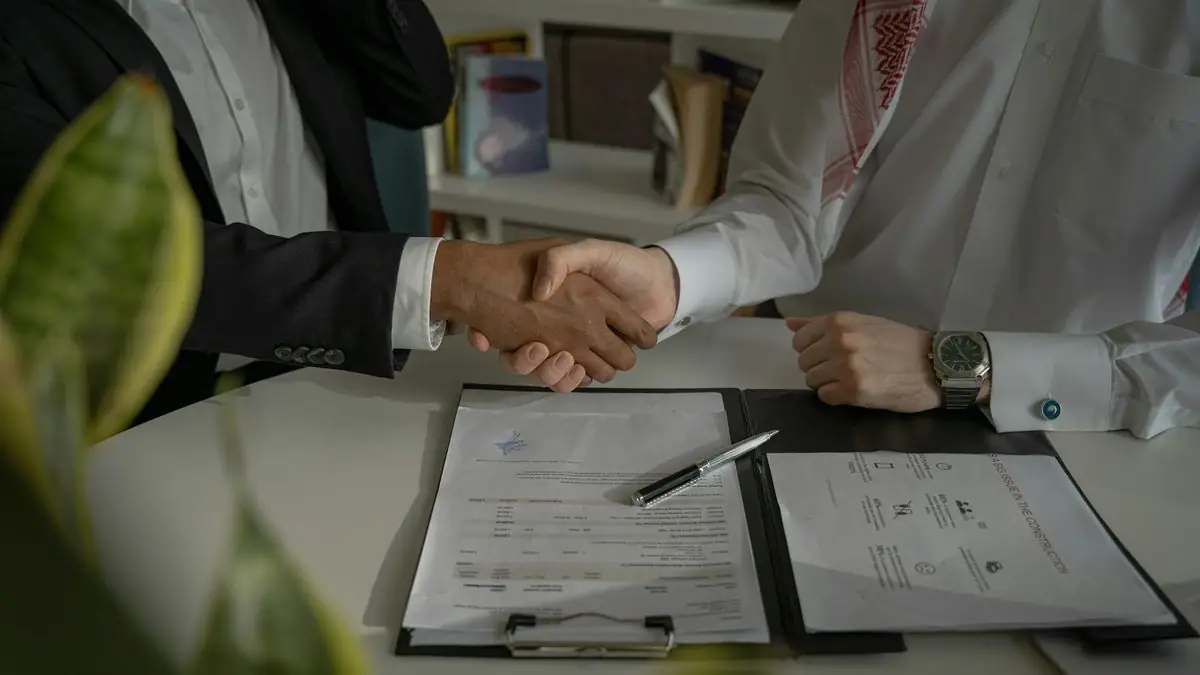 Two people shaking hands over a signed document on a desk