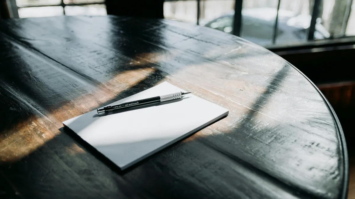 A pen resting on a blank notepad on a dark wooden table