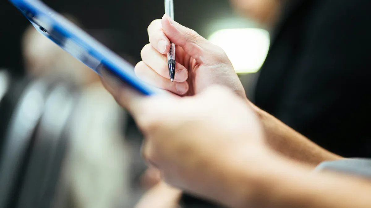 A hand holding a pen over a blue clipboard