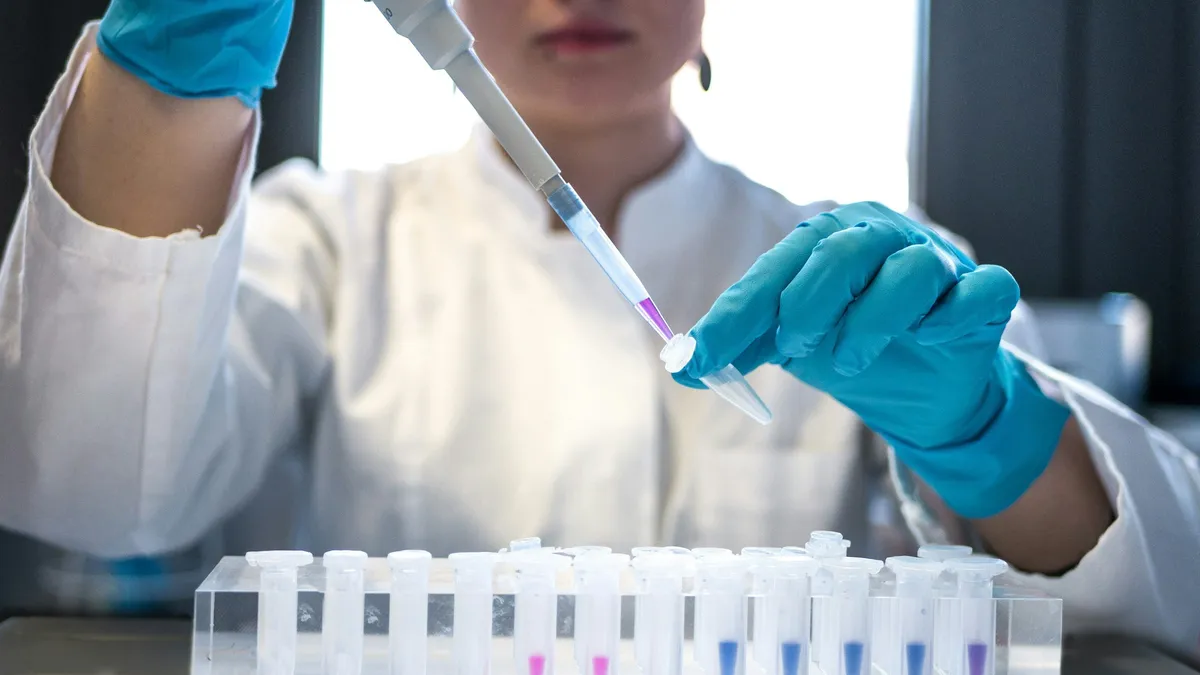 Scientist in gloves pipetting samples into a row of test tubes