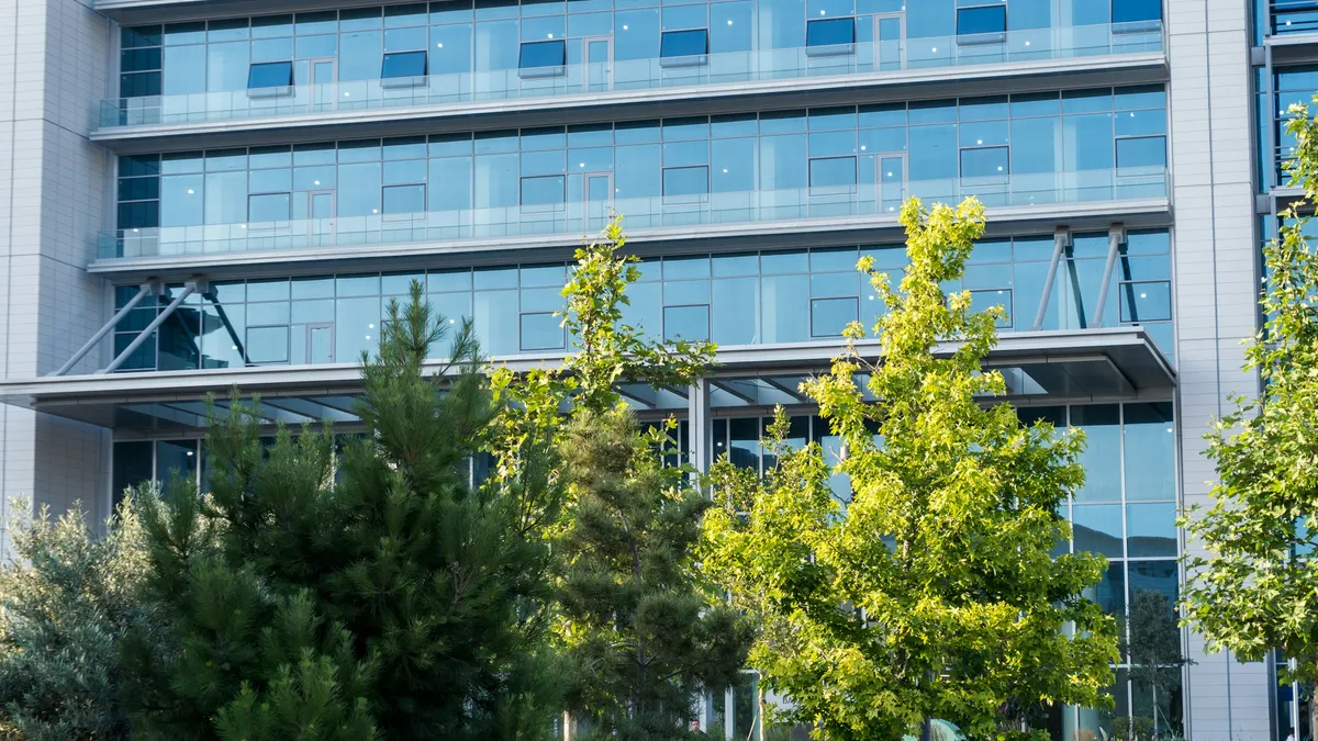 Modern glass office building behind a row of green trees