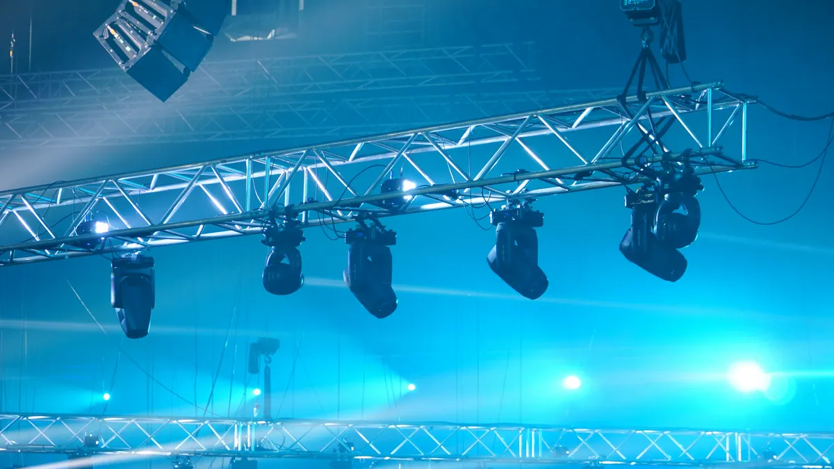 Moving-head stage lights hanging from an aluminum truss in blue light