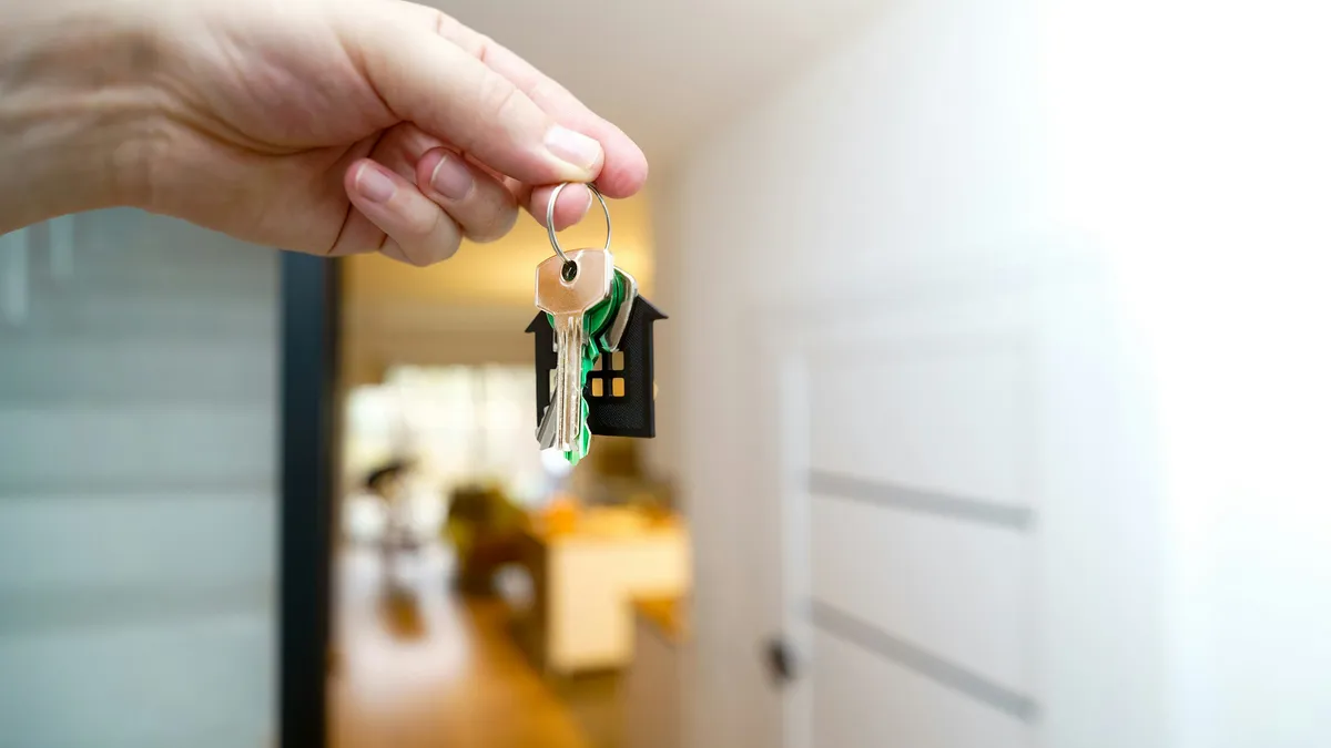 Hand holding house keys in front of a home entrance