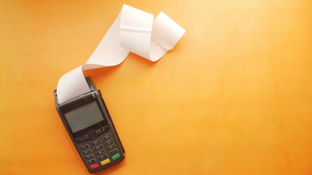 Card payment terminal printing a long receipt on an orange surface