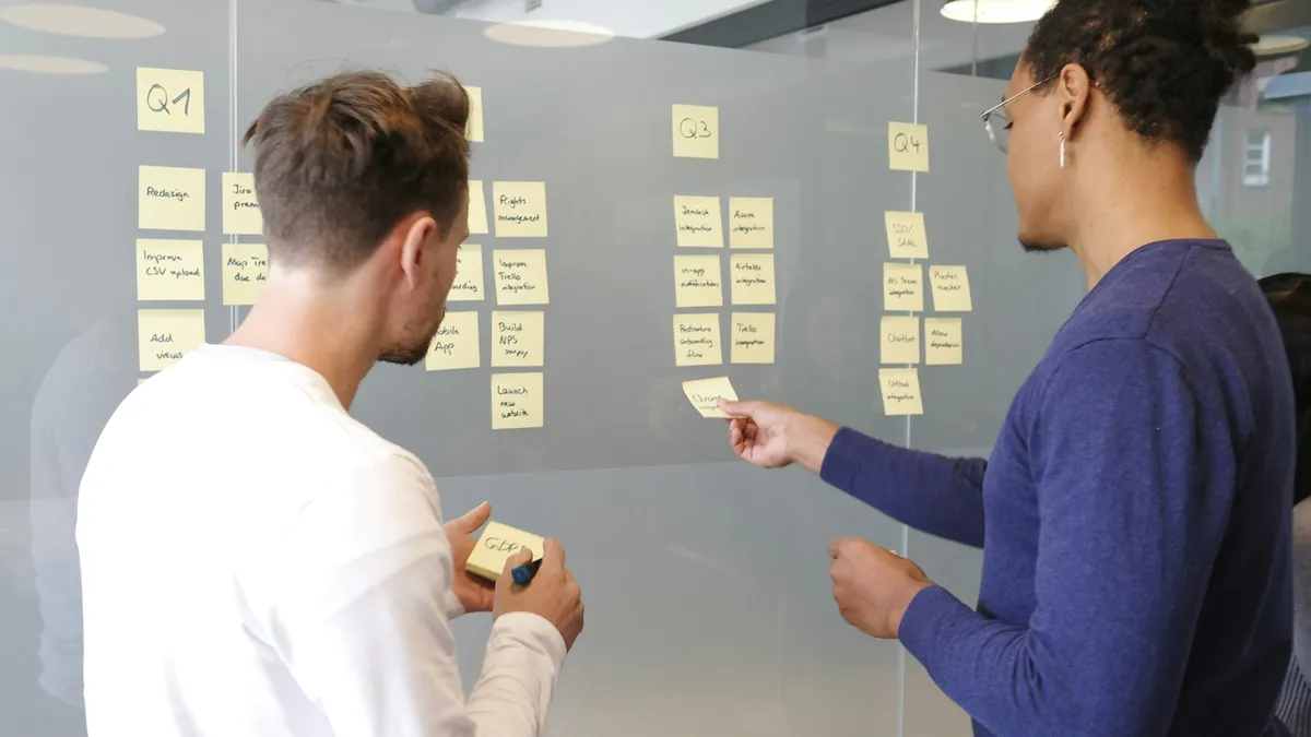 Two consultants planning work with sticky notes on a glass wall