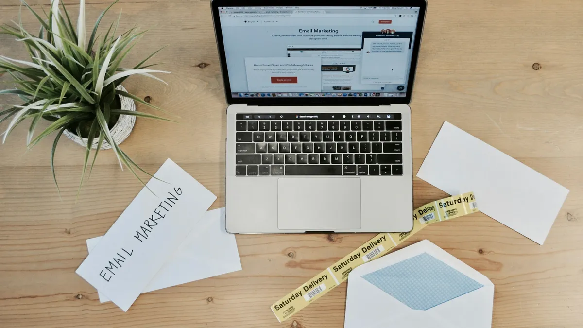 Laptop on a desk beside envelopes and a note reading email marketing