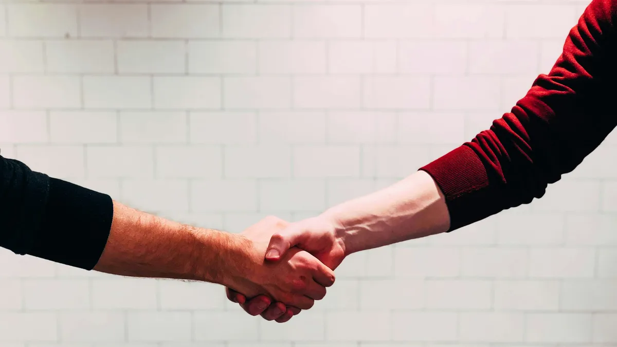 Two people shaking hands against a white tiled wall