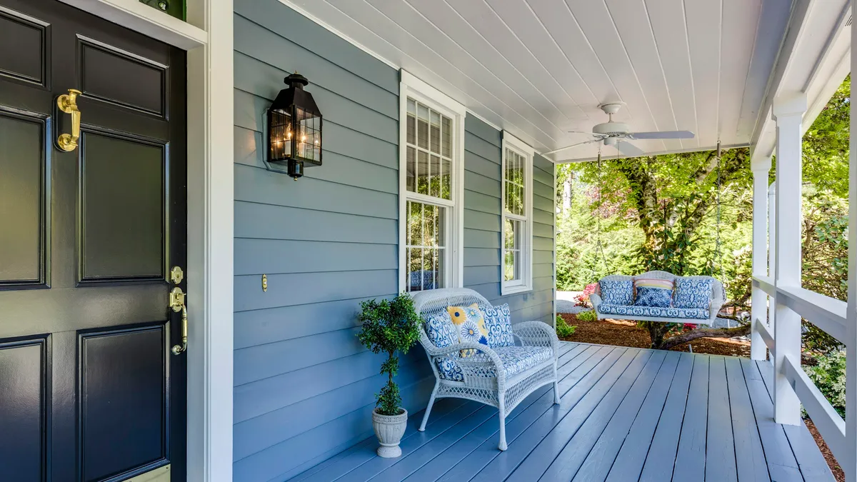 Blue front porch with a black door and white wicker chair