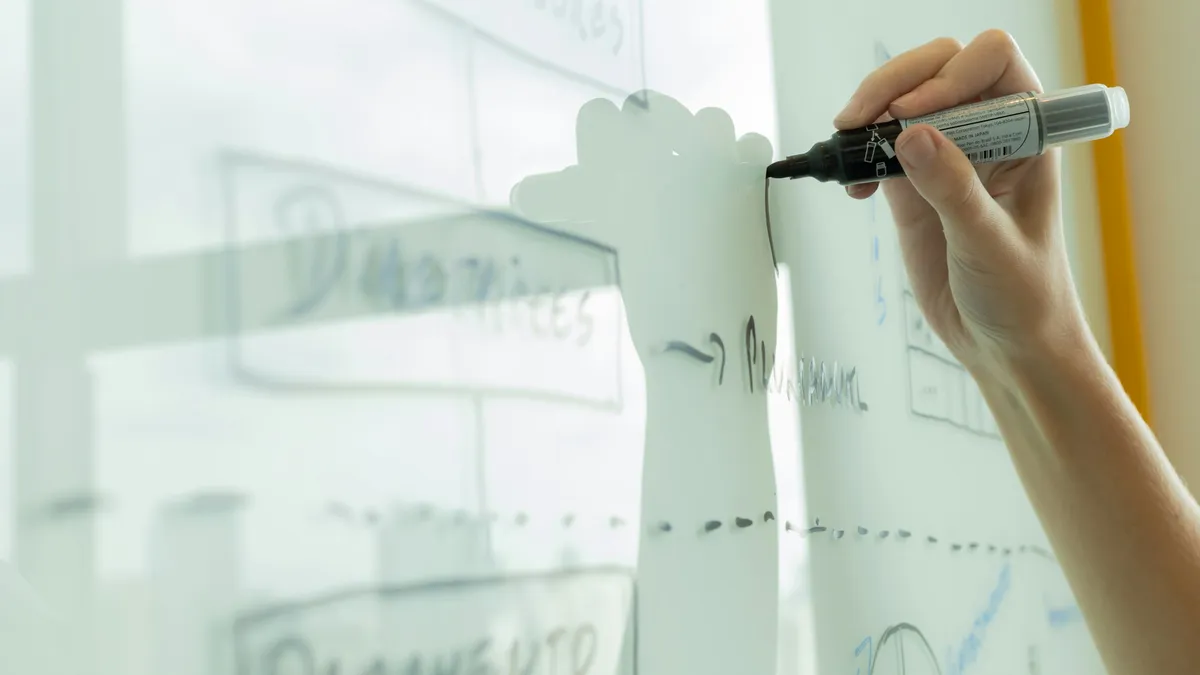 A hand drawing a process diagram on a whiteboard