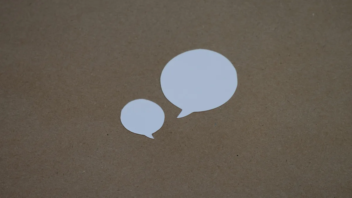 Two blank paper speech bubbles on a brown surface